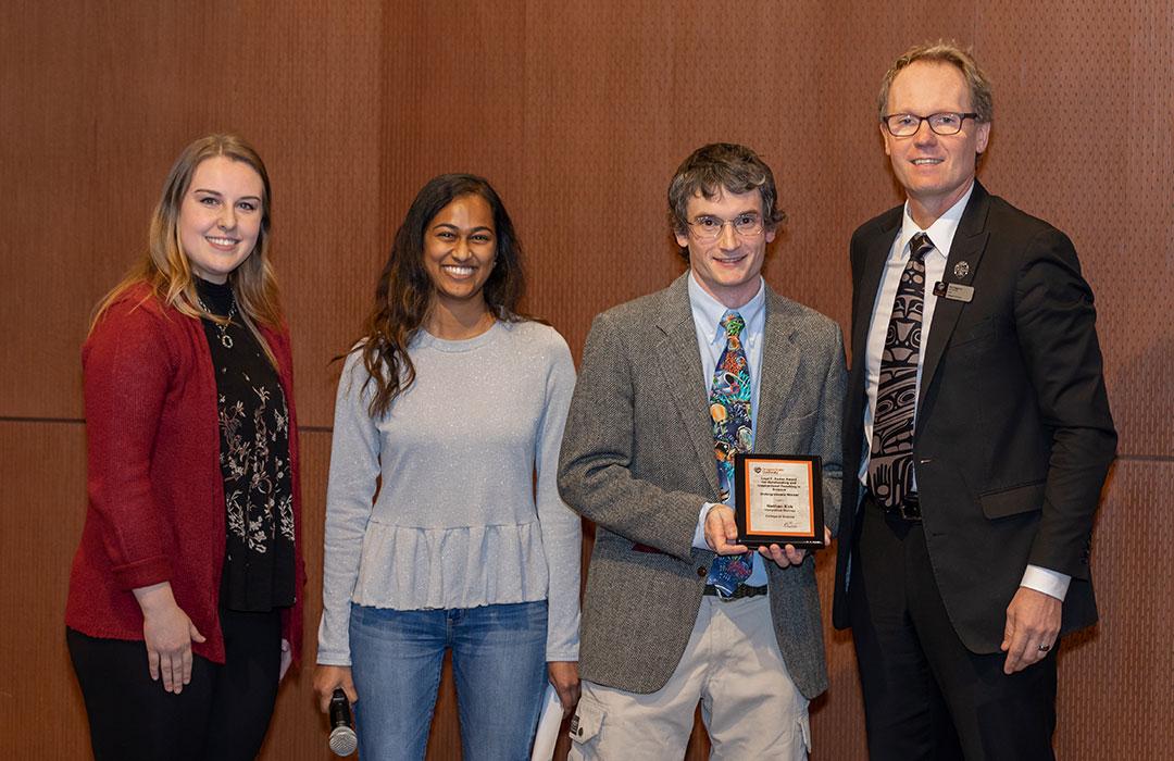 Nate Kirk receiving award from two female students and Roy Haggerty