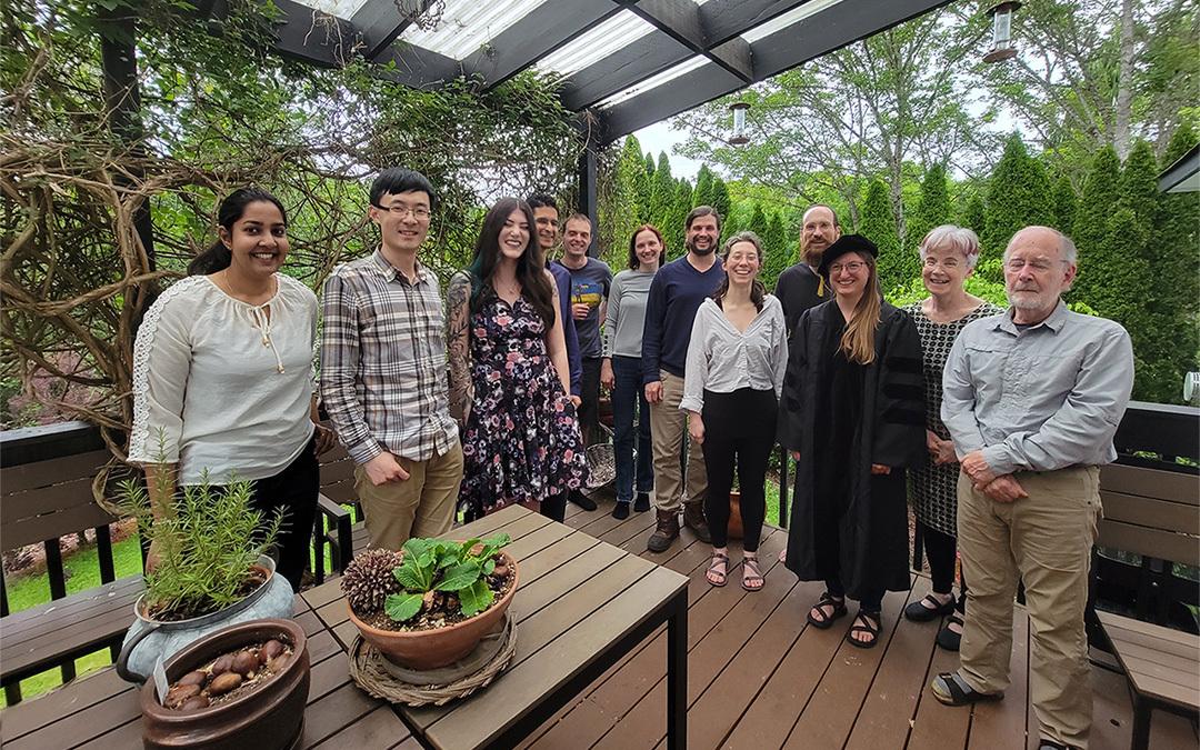 A group of people stand on a deck celebrating the graduation of a postdoc.