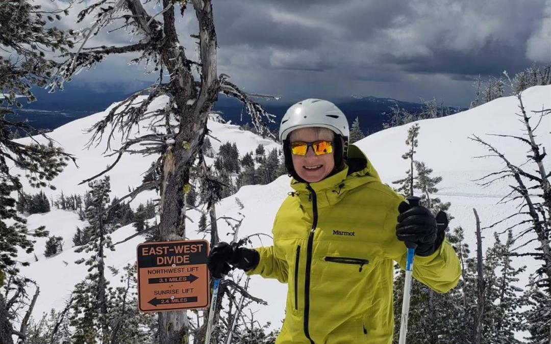 A woman in a skiing outfit stands next to a sign read "East, West."