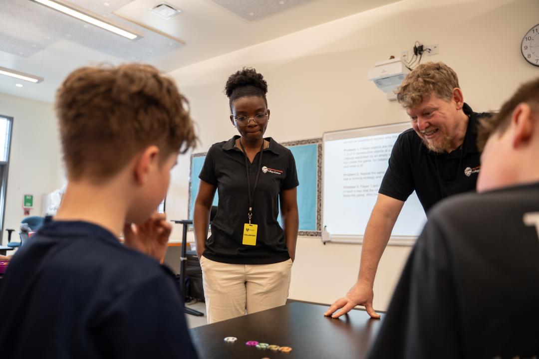 A woman and man talk to two students doing math.