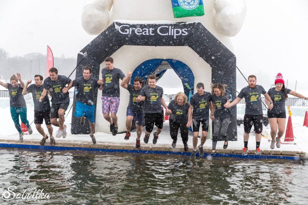 A group of people hold hands and jump into a lake for a polar plunge.