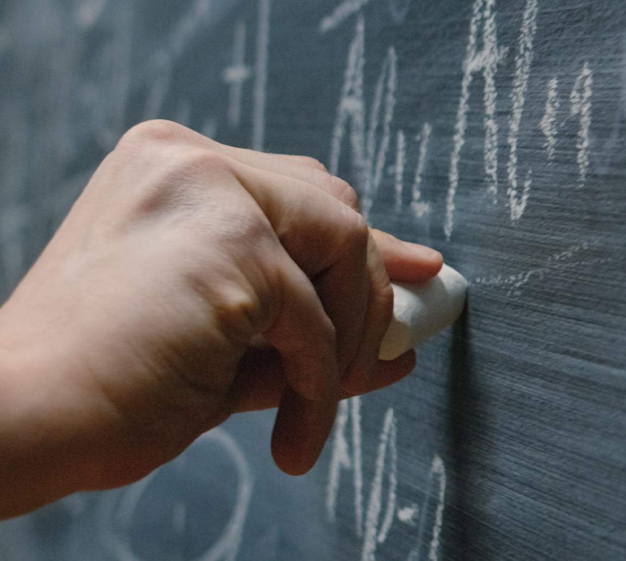 Photo of a hand writing math equations on a chalk board