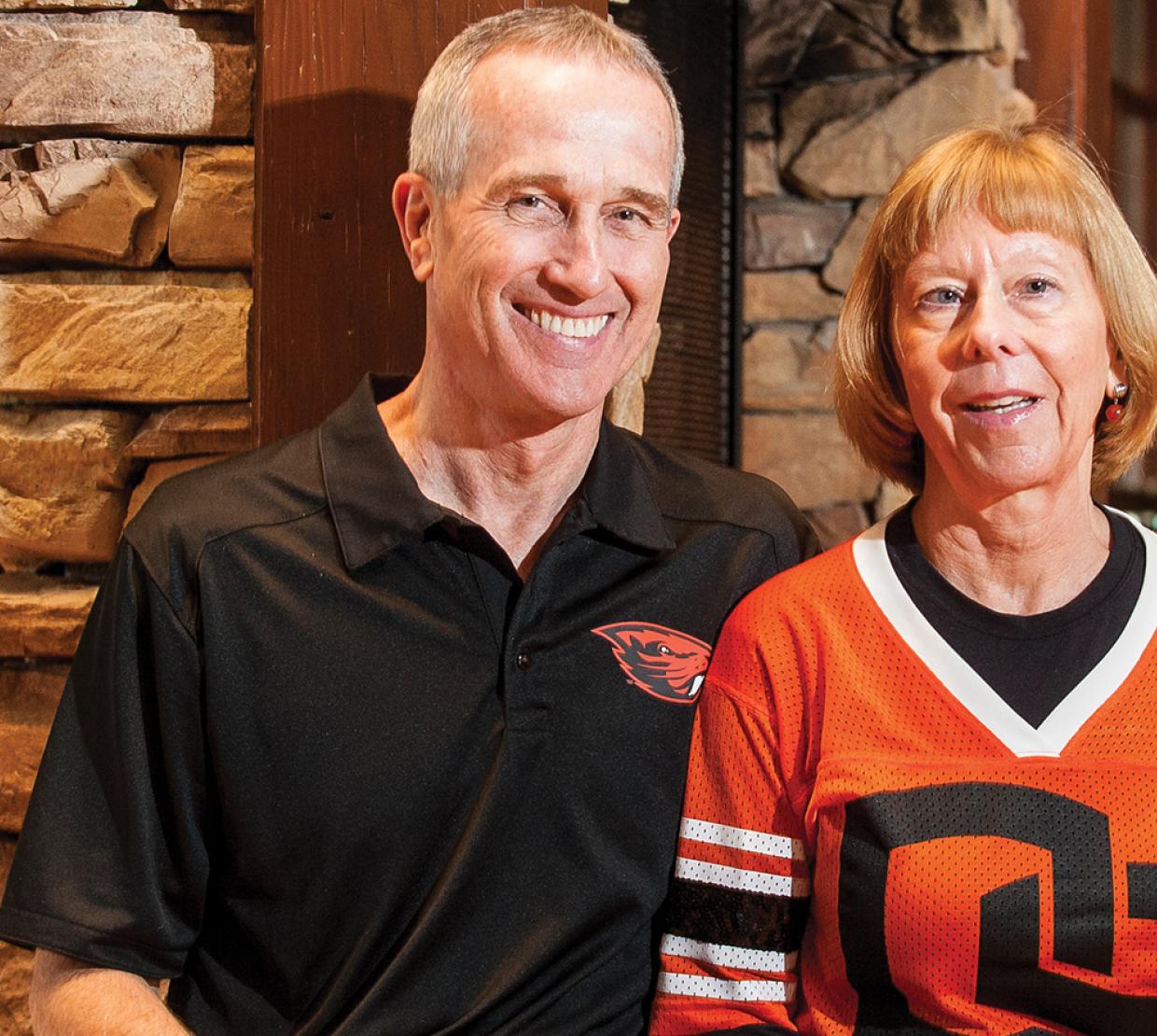 Bernard and Suzanne McGrath sit together in a home wearing Oregon State attire.