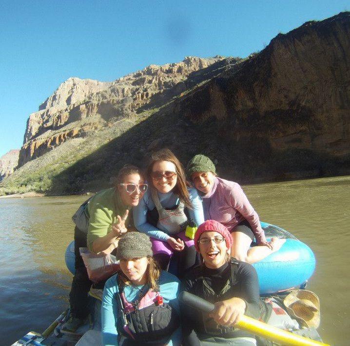 Mary Tunstall gives a peace sign while smiling with a group of friends on a raft in a river.