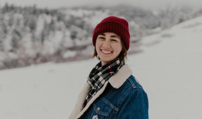 Megan Tucker smiles widely, her scarlet beanie a striking contrast to the snow-covered mountaintops that rise behind her.