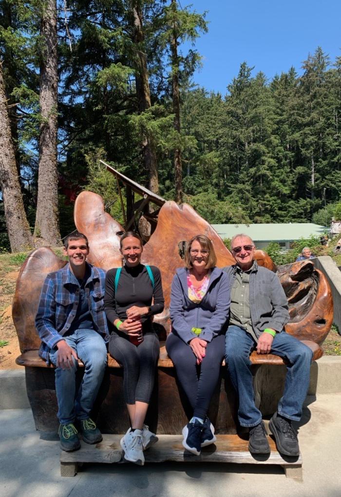 Four people sit and pose for a photo in front of trees.