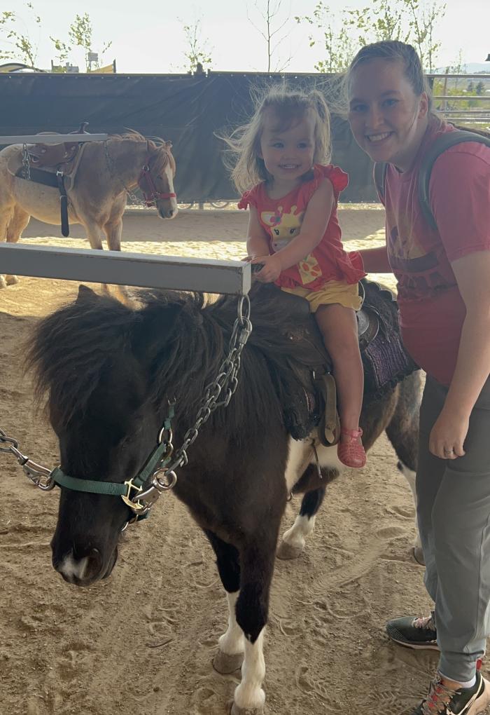 A woman poses for a photo with a young girl sitting on a miniature horse.