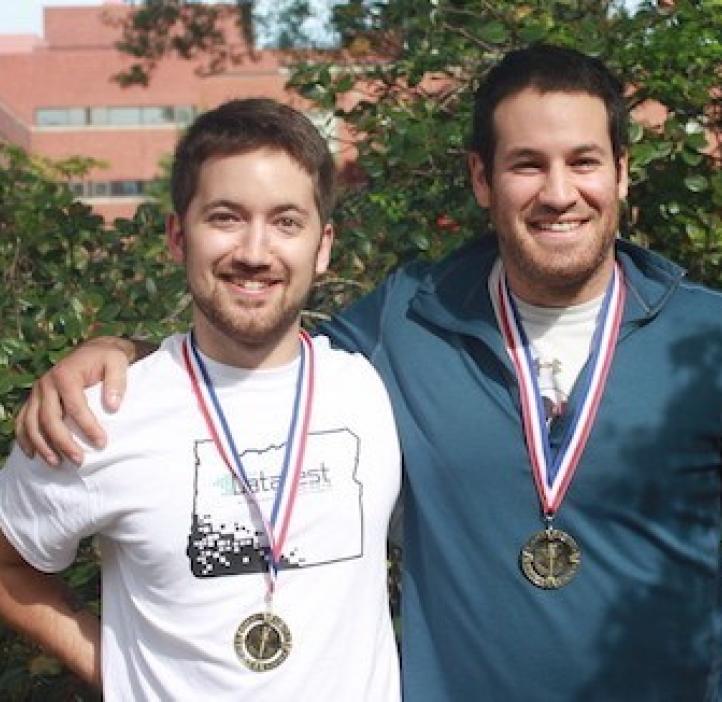 two male students wearing medals in front of shrubbery